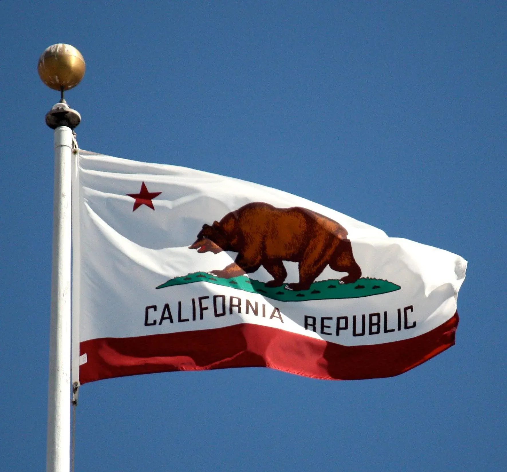 The California Republic state flag and the United States flag flying side by side against a clear sky — Odin Systems provides mobile and permanent video security across all of California.