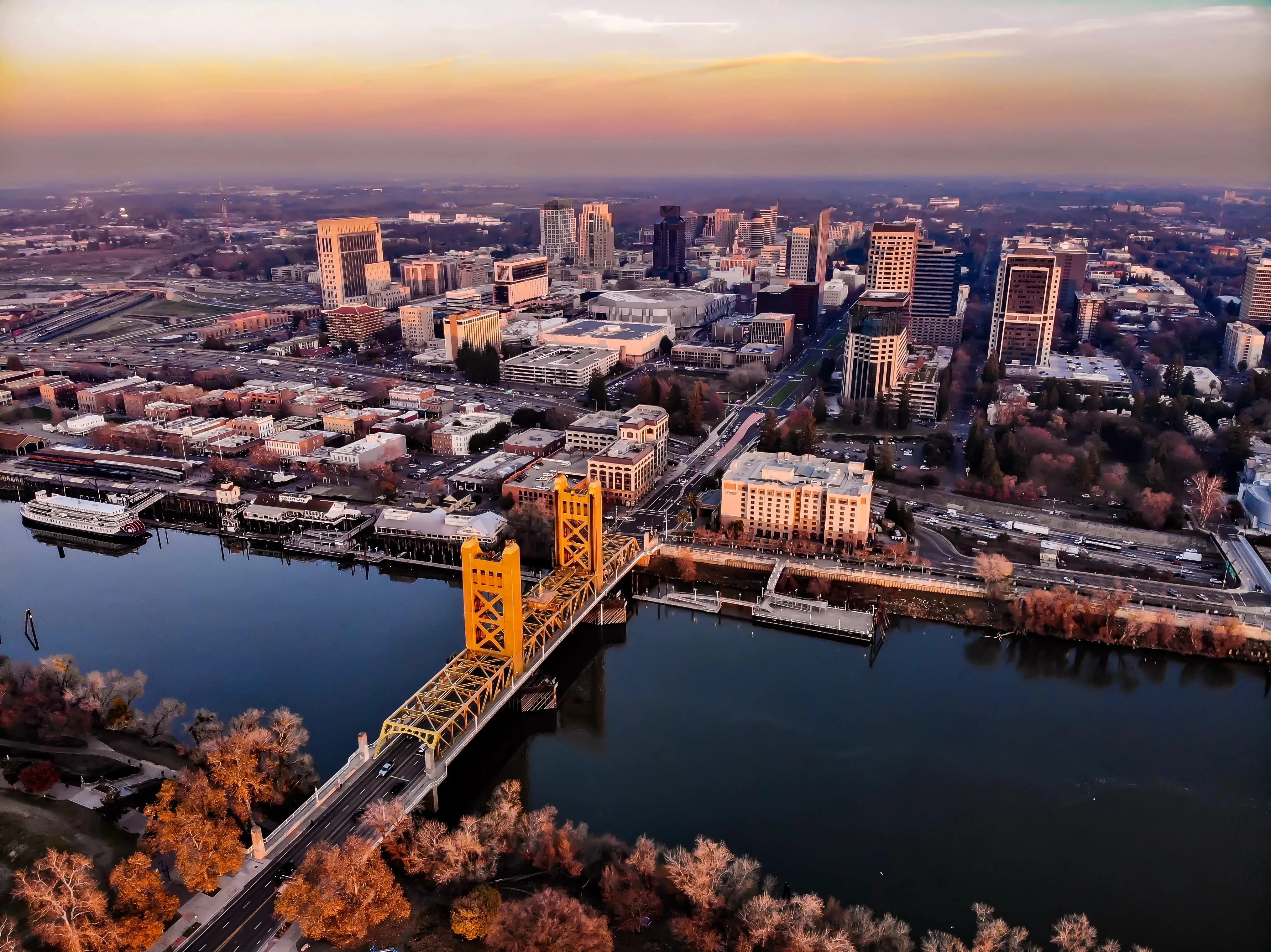 An aerial view of downtown Sacramento at sunset with the Tower Bridge spanning the river and the city skyline beyond — Odin Systems designs and deploys city-wide video security systems across California.